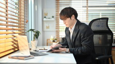 Millennial asian man manager in suit using laptop and planning work projects in bright office.