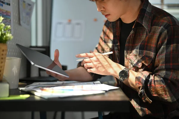 Cropped shot of web developer using digital tablet, working on mobile application software design project at his workstation.