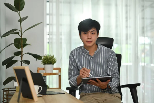 照片中英俊的亚裔男子自由职业者坐在办公室上网 在数字平板电脑上查看电子邮件 — 图库照片