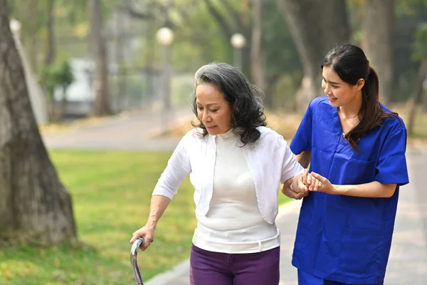Genç Şefkatli Bayan Hemşire Parkta Yürüyen Yaşlı Kadına Yardım Ediyor — Stok fotoğraf