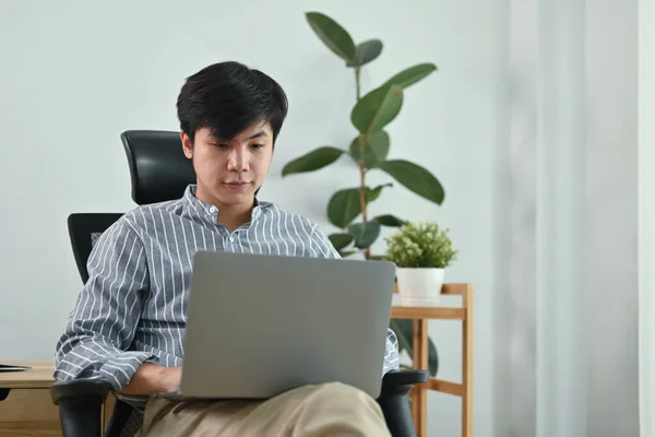 穿着时髦休闲装的英俊男子自由职业者坐在家里办公室里用笔记本电脑的画像 — 图库照片