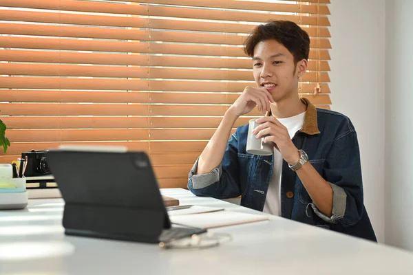 Pleased Young Asian Man Jeans Jacket Drinking Coffee Reading Online — Φωτογραφία Αρχείου