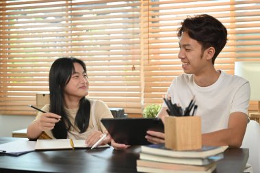 Gülümseyen ağabey ev ödevlerini anlatıyor, küçük kız kardeşine ev işlerinde yardım ediyor..