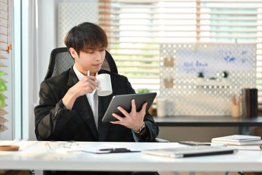 Resmi olarak yakışıklı genç girişimci kahve içer ve ofisinde dijital tablet kullanır..