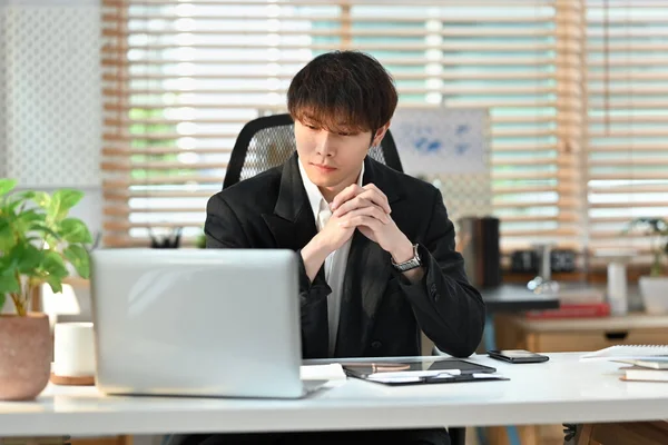 Focused asian male corporate CEO in formalwear watching online presentation on laptop computer.