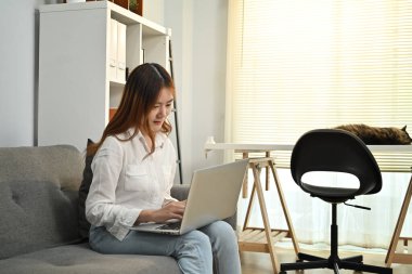 Genç Asyalı kadın internette haber okuyor, evdeki sosyal medyayı kontrol ediyor. İnsanlar, teknoloji ve yaşam tarzı kavramı.