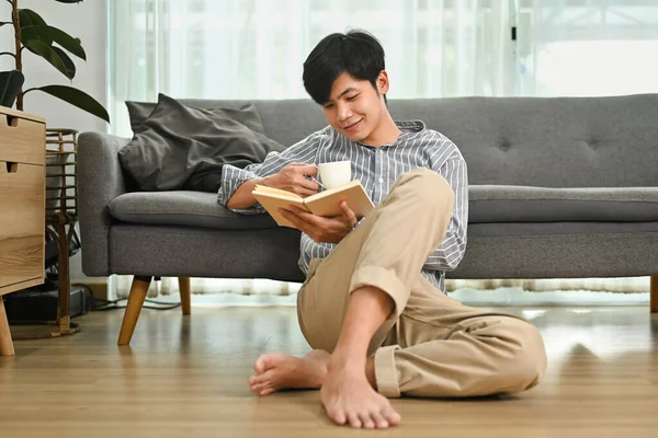 快適なアジアの男の完全な長さが床に座って本を読んで 家で質の高い時間を過ごす — ストック写真