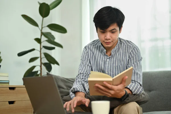 英俊的亚裔自由职业者使用笔记本电脑 并在笔记本上查看他的工作日程计划 — 图库照片