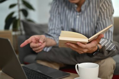 Evinden uzakta çalışırken oturma odasında dizüstü bilgisayar kullanan genç bir adam..