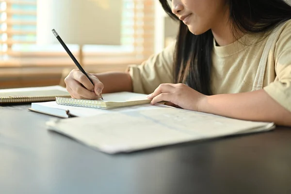 リビングルームのテーブルに座っている間に宿題をするアジアの女の子の書き込みタスクに焦点を当て — ストック写真