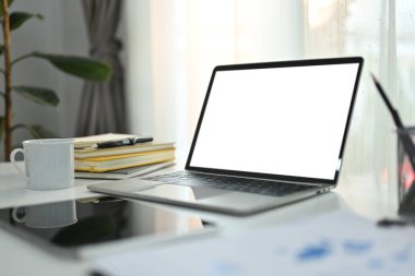 Beyaz beyaz ekranlı dizüstü bilgisayar, beyaz çalışma masasında bir fincan kahve ve dijital tablet.