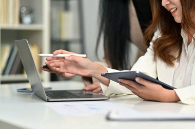 Elinde dijital tablet olan gülümseyen kadın çalışanın görüntüsü ve bilgisayardaki bilgileri meslektaşıyla paylaşıyor..