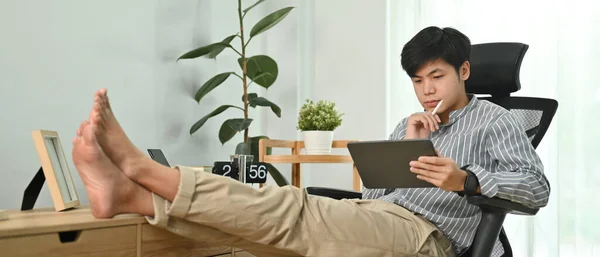 在现代家庭办公室里 即兴自由职业者坐在舒适的椅子上 使用数字平板电脑 — 图库照片