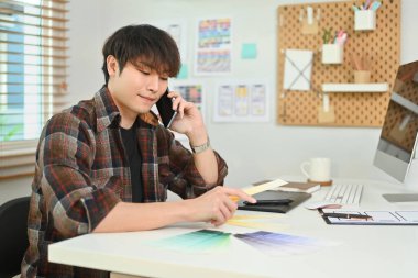 İş yerinde renk örnekleriyle çalışırken cep telefonuyla konuşan şık giyinmiş yaratıcı bir adamın portresi.