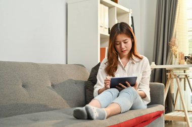 Milenyum kadını kanepede dinleniyor ve dijital tablette internete bakmaktan zevk alıyor. İnsanlar, eğlence ve teknoloji kavramı.