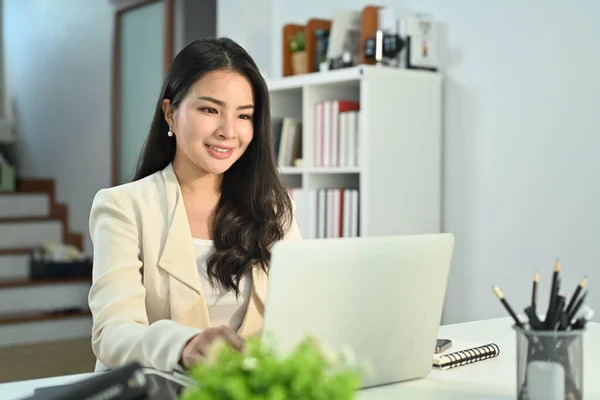 在远离家乡的地方工作时 穿着智能豪华西装的迷人的亚洲女人在笔记本电脑上观看在线网络研讨会 — 图库照片
