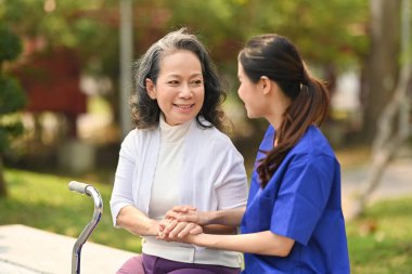 Genç bayan bakıcı yaşlı kadınla konuşuyor, huzurevinde oturuyor. Yardım ve rehabilitasyon kavramı.