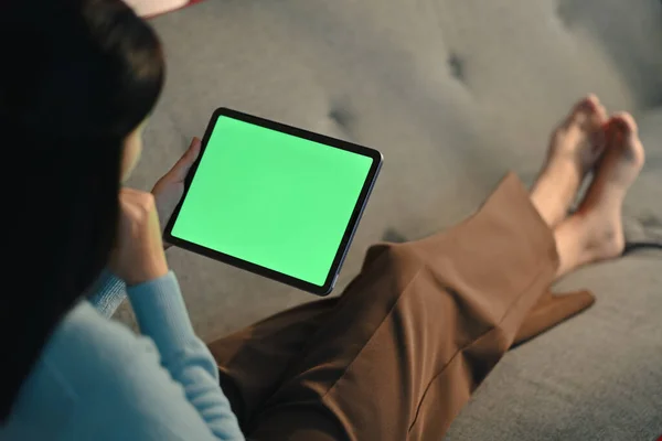 stock image Relaxed woman sitting on couch watching video, surfing internet on digital tablet. Green empty display for your advertising text message.