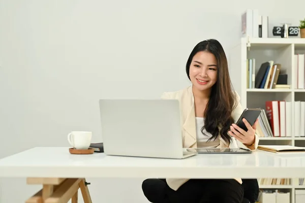 ノートパソコンを使ったアジアの女性セールスマネージャーの笑顔 携帯電話経由でクライアントとの相談 — ストック写真