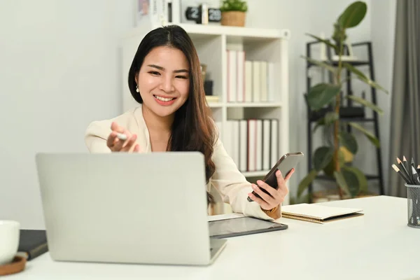 携帯電話を持っている陽気なアジアの女性労働者と通信またはラップトップ上でオンライン監視ウェビナー — ストック写真