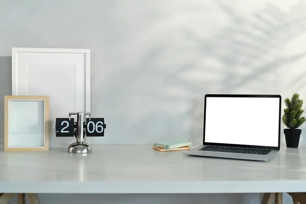 Laptop, vintage flip clock, blank picture frame and houseplant on white table. Copy space for your text.