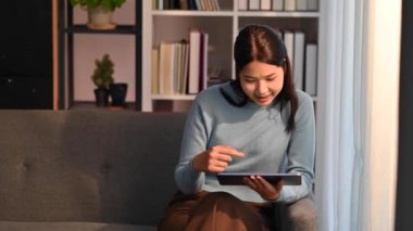 Güzel bir milenyum kadını rahat oturma odasında kanepede oturuyor ve dijital tablet kullanıyor. İnsanlar, teknoloji ve yaşam tarzı.