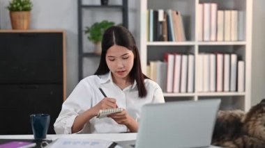 Laptop ekranına bakıp notlar yazan odaklanmış genç bir kız öğrenci. E-öğrenim eğitim kavramı.