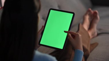 Kanepede dinlenen genç bir kadının arka görüntüsü, yeşil ekran leke telefonuna kayıyor..