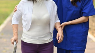 Rehabilitasyon merkezinde yürürken yaşlı bir kadınla ilgilenen bakıcı görüntüsü. Yardım, rehabilitasyon ve sağlık.