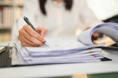 Belgelerde kalem tutan kadın muhasebecinin yakın görüntüsü, masa başı pazarlama raporlarını kontrol etmek.