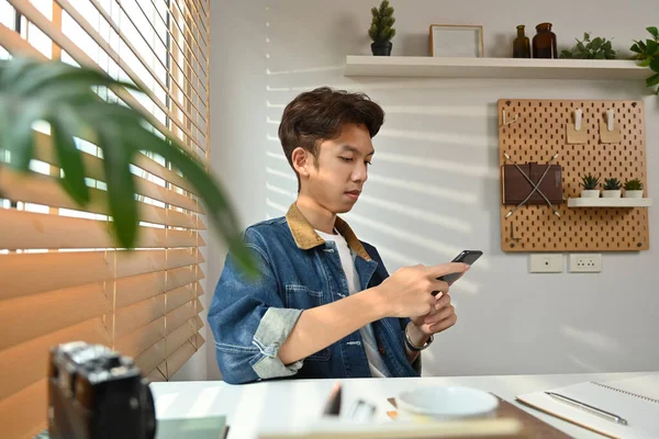 Young hipster man chatting with friends, reading text message, browsing internet on mobile phone.