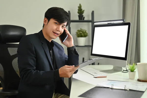 在现代办公室里 快乐的亚洲商人坐在空白的电脑屏幕前 用手机聊天 — 图库照片