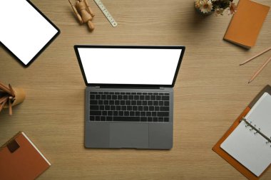 Dizüstü bilgisayarın üstünde, dijital tablet ahşap çalışma masasında kırtasiye malzemeleriyle çevrili..