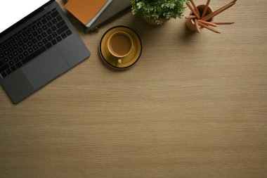 Dizüstü bilgisayar, bir fincan kahve, kalem tutacağı ve ahşap çalışma masasında not defteri. Kopyalama alanı olan üst görünüm.