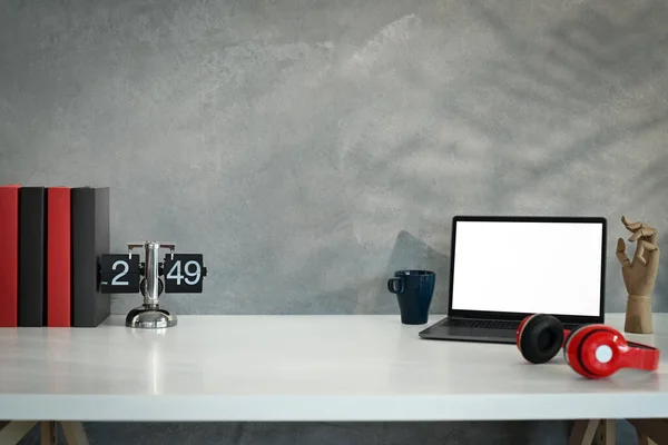 Laptop computer, wireless headphone, vintage flip clock and books on white table against loft wall.