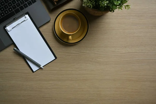 stock image Blank clipboard, cup of coffee and laptop computer on wooden office desk. Top view with copy space.