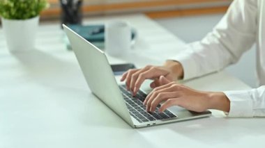 Beyaz ofis masasında laptopun kapağını yazıp kapatan kırpılmış erkek işçi elleri. 