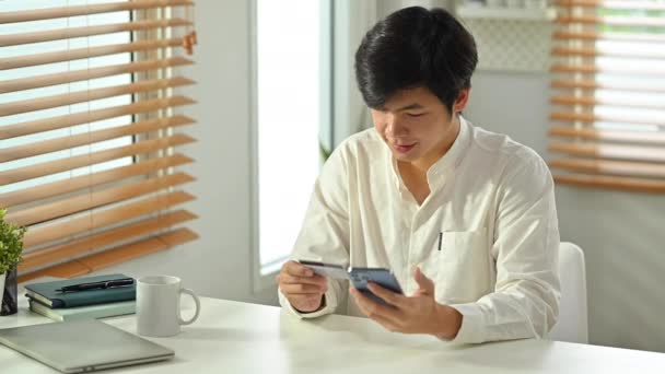 オンライン銀行取引を行う大人のアジアの男性消費者のクレジットカードとスマートフォンを保持笑顔 Eコマース モバイルバンキングのコンセプト — ストック動画