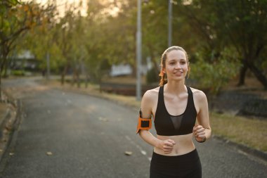 Tropikal parkta akıllı telefon koşusu için kolluk takan mutlu sporcu kadın. Spor ve sağlıklı yaşam tarzı kavramı.