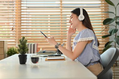 Hoş, genç bir kadın, günlük kıyafetleriyle elinde akıllı bir telefon, kulaklıkla kulaklıkla müzik dinliyor..
