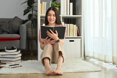 Huzurlu bir milenyum kadını yerde ve oturma odasında en sevdiği romanı okuyor. İnsanlar, eğlence ve yaşam tarzı konsepti.