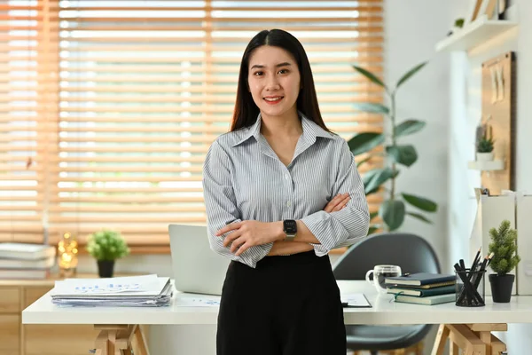 美しいビジネス女性の肖像画は 彼女の作業机の前に腕を身に着けて立って カメラで微笑む — ストック写真