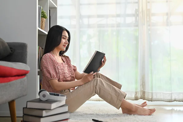 漂亮的女人坐在客厅的地板上看书 周末在家里消磨时光 — 图库照片
