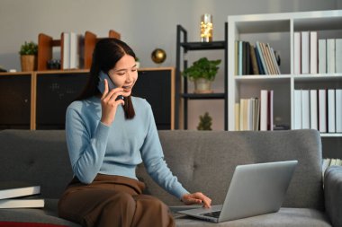 Güzel bir kadın güzel bir telefon görüşmesi yapıyor ve kanepede dizüstü bilgisayar kullanıyor. İnsanlar, iletişim ve teknoloji.