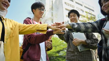 Bir grup üniversite öğrencisi dışarıda el ele tutuşup kutlama yapıyor. İlişki gençliği ve toplum kavramı.