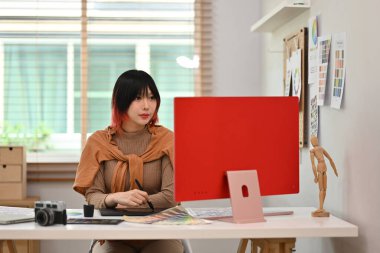 Güzel genç bayan tasarımcı grafik tableti kullanıyor ve yaratıcı çalışma istasyonunda renk örnekleriyle çalışıyor..