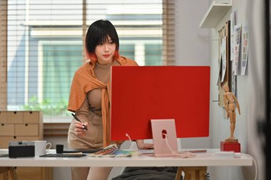 Grafik tablet kullanan ve yaratıcı çalışma istasyonunda renk örnekleriyle çalışan genç kadın tasarımcının portresi.