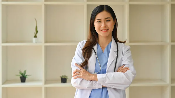 stock image Positive female doctor in white coat with stethoscope standing with arms crossed and smiling at camera. Healthcare and medical.