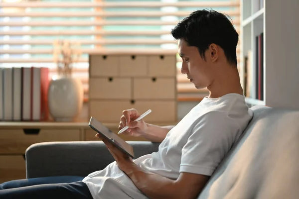 Kanepede Oturup Dijital Tablet Kullanan Asyalı Bir Adamın Yan Görüntüsü — Stok fotoğraf