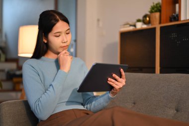 Kanepede oturmuş dijital tablette kablosuz interneti karıştıran gülümseyen yetişkin bir kadın. Teknoloji, insanlar ve yaşam tarzı kavramı.